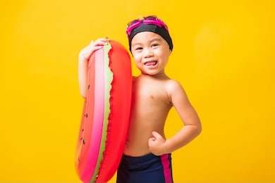 summer vacation concept, portrait asian happy cute little child boy wear goggles and swimsuit hold watermelon inflatable ring, kid having fun on summer vacation, studio shot isolated yellow background