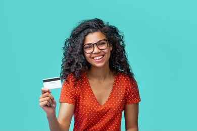 close up portrait of attractive girl with prfect smile holding credit card in hand over bright blue background.