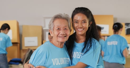 portrait of female volunteer and her mother posing with attractive smile to camera. volunteer, social support and donation concept.