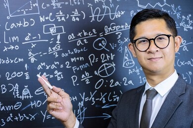 asian teacher wears glasses and wears a black suit. standing in front of a black body with mathematical formulas