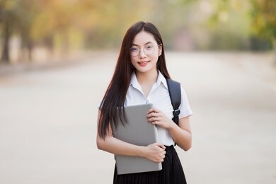 young teen female asian university student with bagpack holding laptop in the university campus. female university student go to university. back to school concept.