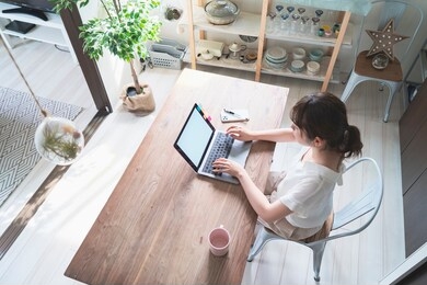 asian woman doing remote work with laptop at dining table at home
