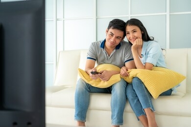 asian happy fcouple sitting in sofa and watching television at home concept of family values, vacation day, holiday, happiness or lifestyle.