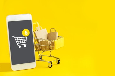 mobile shopping. basket with grocery paper bags, boxes, phone with a shopping icon, on a yellow isolated background. close-up, copy of the space