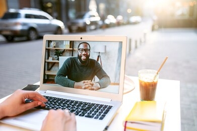 video call. webcam shot young black guy on the laptop screen, two friends have video chat in summer cafe outdoors