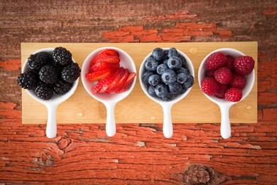 fresh assorted berries on a grungy wooden counter displayed in small ceramic ramekins including blackberries, blueberries, strawberries and raspberries for a healthy snack or appetizer