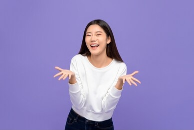 smiling cheerful cute asian woman in casual attire doing blow a kiss gesture with open palms isolated on purple studio background
