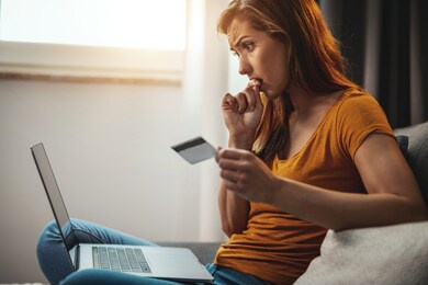 worriedly young woman doing online shopping on her laptop while sitting on the sofa at home.