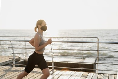 young beautiful woman runs early in the morning. the beginning of a new day. active lifestyle. a black face shield is worn on the face. protection against diseases and viruses.