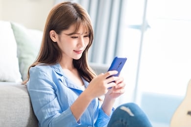 asian young woman is using smart phone and lying on couch leisurely in living room at home
