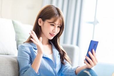 asian young woman has video chat with friends with smart phone in living room at home