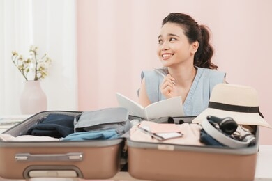 preparing suitcase for summer vacation trip. young woman checking accessories and stuff in luggage at home before travel.