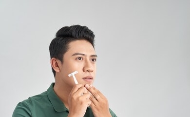 young man is passing the razor for the beard while it looks at the mirror