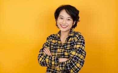 young beautiful asian woman with short hair wearing casual plaid shirt over yellow background happy face smiling with crossed arms looking at the camera. positive person.