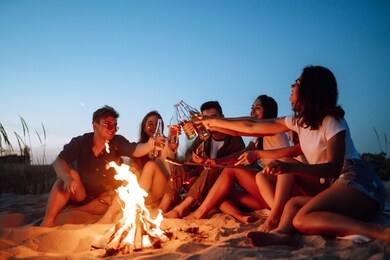 group of happy friends  cheers and drink beers on the beach, enjoying vacation. vacation time laughing and smiling.