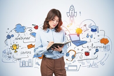 beautiful young european woman writing in notebook near blue wall with colorful online education sketch drawn on it. concept of e learning