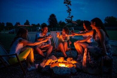 friends enjoying evening drinks by firepit outdoors.