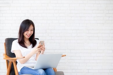 young asian woman is freelance sitting using working on smartphone and laptop computer, free time of girl relax and cozy on phone with happy and comfort, business and technology, lifestyle concept.