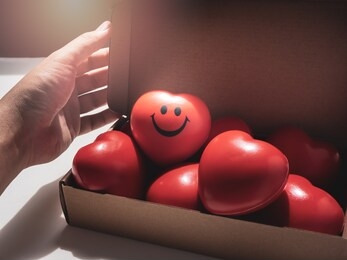 hand opening brown paper craft box with red hearts with happy and smiling face on many red ball foam with heart shape inside. love, care, share, donation and valentine day concept.