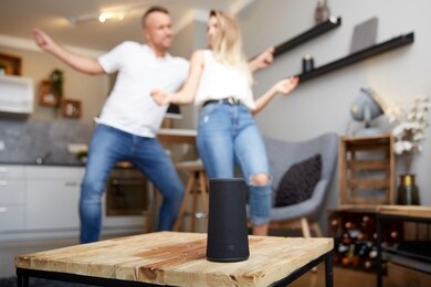 close-up of smart speaker on wooden table against happy couple dancing in living room at home