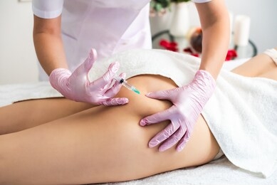 correction of body fat with lipolytics. in the cosmetologist s office, female hands in pink gloves inject a young woman in the thigh. white canvas. healthy body concept, slim body.