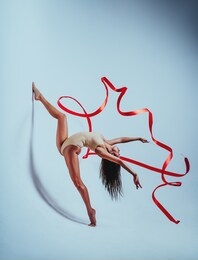 young woman gymnast dancing with red ribbon on white background