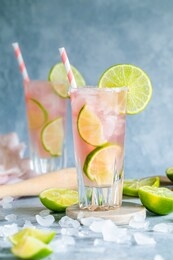 a fresh cocktail drink with lime and pink grapefruit juice. paloma cocktail. two glasses on the table and they have environmentally friendly paper straws. blue gray background with copy space.