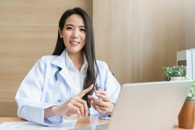 young attractive asian female doctor diagnosis talking and looking to camera in video conference ,positive doctor waving and having online consultation on digital tablet laptop