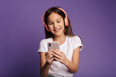 photo of laughing attractive girl using wireless headphones and mobile phone isolated over purple background