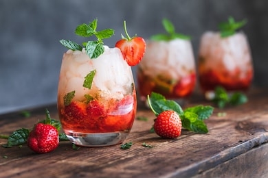 fresh strawberry mojito drinks. there are three drinks on a vintage wooden dark table.  the cocktails or mocktails are decorated with strawberries and fresh mint. copy space room for text.