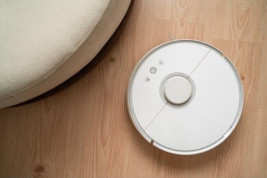 robot vacuum cleaner removes dust in room on brown floor. vacuum cleaner in ordinary apartment. modern household wireless device for cleaning house. smart home concept