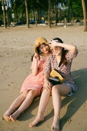 two cute girls sitting together on the beach in the evening sunlight.