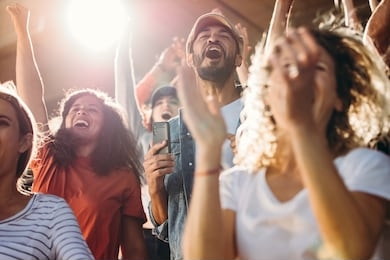 large group of football fans in stadium yelling and cheering with excitement for their team. excited sports fans standing with their hands raised and celebrating their team's victory.