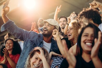 group of supporters watching football game and making self-portrait with smartphone at stadium. multi-ethnic people enjoying watching a game at stadium and taking a selfie.