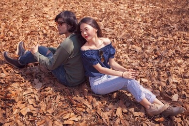 young asian couple sitting on dry leaves ground