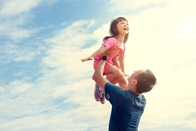 family holiday the sky is bright. father and daughter are playing outdoors happily. father carried his daughter and lifted him up into the sky.the daughter acted with arms outstretched to fly happily.
