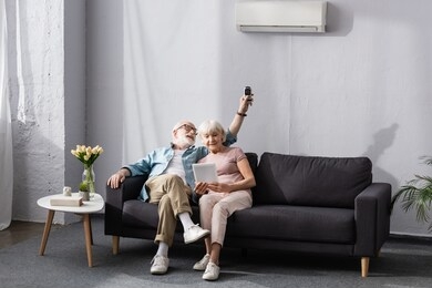 senior woman using digital tablet near smiling husband switching air conditioner with remote controller