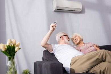 selective focus of smiling man switching air conditioner with remote controller near wife