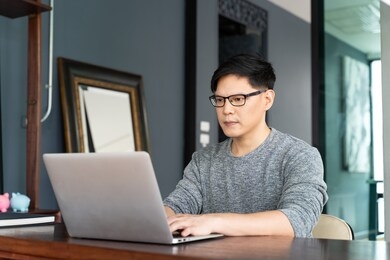 confident busy asian male freelancer in eyewear working on laptop computer at moder home.