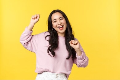 people emotions, lifestyle leisure and beauty concept. upbeat happy and cheerful asian girl dancing and having fun, partying, moving rhythm music and smiling over yellow background