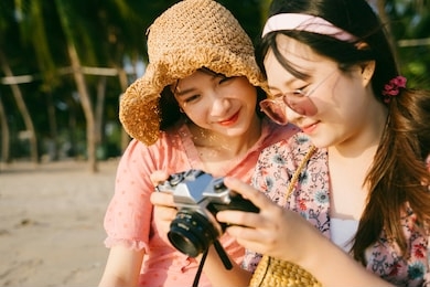 two girls sitting on the beach and look at the photo of this trip.