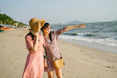 two girls standing on the beach, girl in sunglasses point to the beautiful boat in the sea.