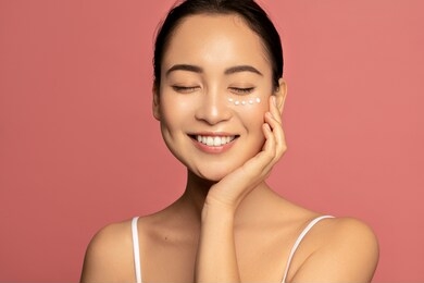 anti aging eye cream. young beautiful model posing aginst pink background with applyed cream under her eyes