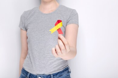 world hepatitis day concept. girl in gray t-shirt holds in her hand awareness symbol red-yellow ribbon. gray background. copy space