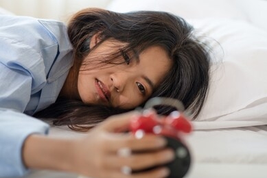 young asian woman laying on bed and watching her alarm clock in the morning