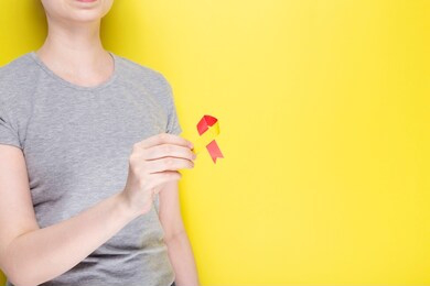 world hepatitis day concept. girl in gray t-shirt holds in her hand awareness symbol red-yellow ribbon. yellow background. copy space