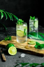 fresh mojito cocktail with lime, mint and ice in a glass jar on a black background and a wooden board. summer cold drink and cocktail. selective focus.