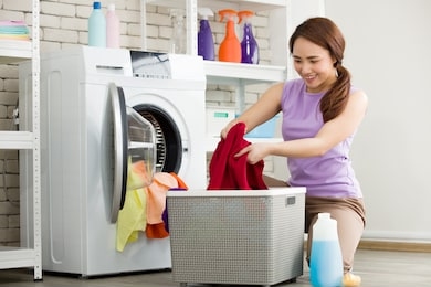 asian housewife is separating clothes from the basket and put them into the washing machine for laundry. young woman is happily doing housework.