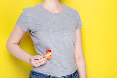 world hepatitis day concept. girl in gray t-shirt holding red-yellow ribbon area liveras symbol of awareness. yelow background