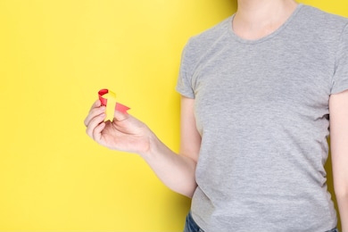 world hepatitis day concept. girl in gray t-shirt holds in her hand awareness symbol red-yellow ribbon. yellow background. copy space